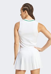 Top blanco sin mangas con un cuello verde y falda blanca con pliegues. La tela es texturizada, ligera y diseñada para la ropa activa.