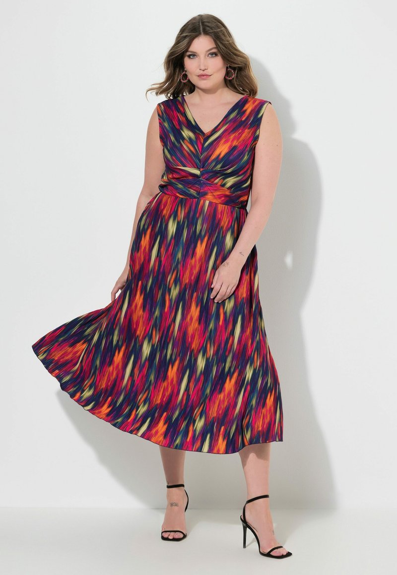 Värikäs maxi-mekko, jossa on olkaimettomuus, V-aukko, kiertävä yksityiskohta vyötäröllä ja lainehtiva hame kirkkaalla abstraktilla kuviolla.
