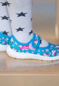 Blauwe kinderschoenen met een eenhoornpatroon, roze accenten en een klittenbandsluiting. Draagt met grijze sokken versierd met zwarte sterren.