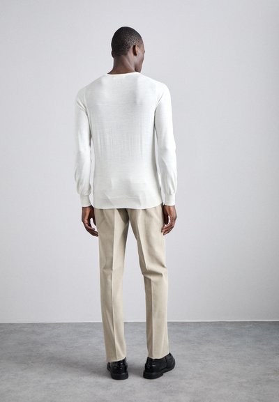 Leichter, off-white gestrickter Pullover mit langen Ärmeln, Rundhalsausschnitt und strukturiertem Finish, kombiniert mit beigen geraden Hosen und schwarzen Schuhen.