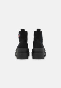 Czarne kanwy botki za kostkę z grubymi czarnymi gumowymi podeszwami, krótkimi pętelkami z tyłu i małą łatą z logo z boku.