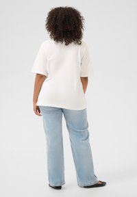 T-shirt blanc à manches courtes avec une coupe décontractée, associé à un jean droit bleu clair. Le jean a une texture en denim doux et peu de détails.