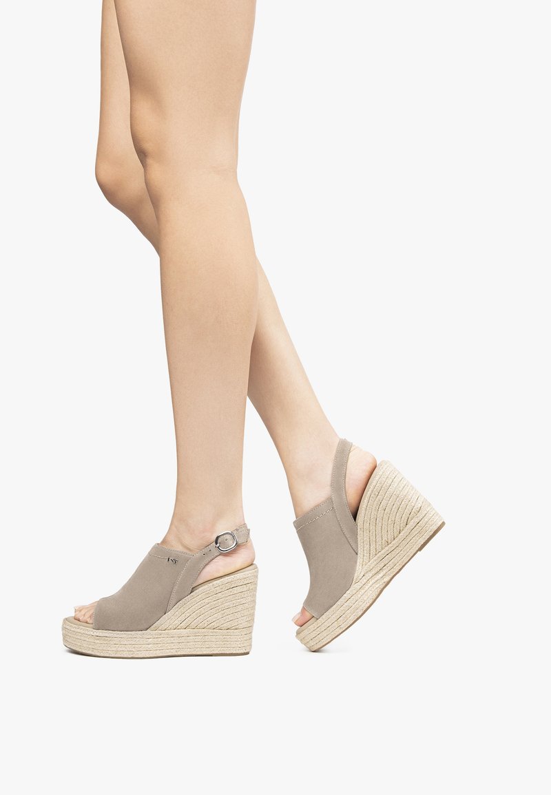 Beige suede wedge sandals with a peep toe, a slingback design, and a textured jute platform. Features a silver-tone buckle accent.