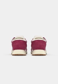 Pink and maroon suede sneakers with white accents and a beige sole. Features "CONVERSE" branding on the heel. Flat lace-up design.
