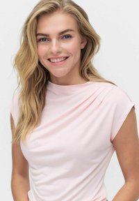 Vaaleanpunainen t-paita pehmeästä kankaasta, jossa on laskostettu muotoilu kaula-aukolla ja lyhyet hihat, joissa on vähäiset ompeluyksityiskohdat.