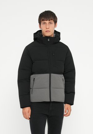 Padded jacket with a black top half and gray lower half, featuring a hood, front zip, and two side pockets. Textured fabric for warmth.