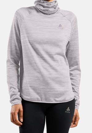 Woman wearing light gray long-sleeve athletic top with high neck and black leggings, both with Odlo brand logos visible.