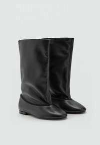 Botines de cuero negro con un eje suave y caído. Diseño de tacón plano y punta afilada. Textura lisa con una estética minimalista.