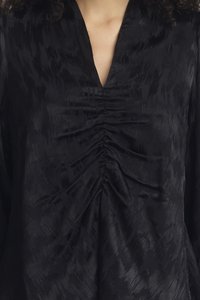 Blusa nera con scollo a V profondo e tessuto texture. La parte frontale presenta dettagli arricciati, creando un effetto drappeggiato.