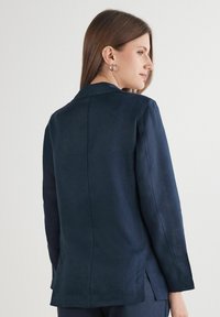 Mörkblå lin skjorta med krage, långa ärmar och rak bakdesign. Har sidofå längst ner och en ren, texturerad finish.