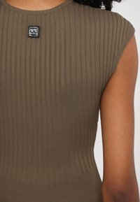 Brown ribbed sleeveless top featuring a rounded neckline and a small black label near the shoulders. Soft, stretchy fabric with a smooth texture.