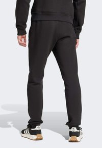 Svarta mjukisbyxor i mjukt tyg med avsmalnande design, elastisk midja och ribbade muddar; kombinerade med svartvita träningsskor.