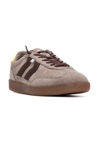 Zapatillas de ante en gris claro con rayas marrón oscuro, cordones marrones y suela de goma; cuenta con un acento amarillo en el talón.