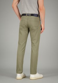 Olivengrüne Slim-Fit-Hosen mit Gesäßtaschen, aus Baumwollmaterial und mit glatter Textur. Kombiniert mit weißen Sneakers und einem grauen Hemd.