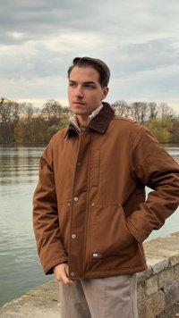 Brown insulated jacket with a corduroy collar, two front pockets, silver snap buttons, and a relaxed fit, worn over a light beige top.