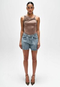 Bruine mouwloze top met een gedraaide ontwerp, gecombineerd met lichtblauwe denim shorts. Model draagt puntige hakken; minimaal patroon op de kleding.