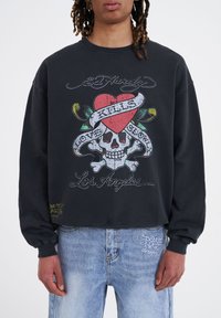 Svart kortärmad sweatshirt med en grafik som visar ett skalle, ett hjärta och text. Texten inkluderar "Ed Hardy", "Love Kills" och "Los Angeles".
