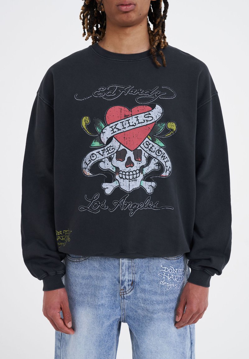 Svart kortärmad sweatshirt med en grafik som visar ett skalle, ett hjärta och text. Texten inkluderar "Ed Hardy", "Love Kills" och "Los Angeles".