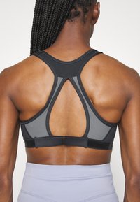 Black and gray sports bra with a textured design, racerback style, and adjustable band. Features a sleek fit and breathable material.