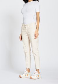 Body ajustado de manga corta blanca combinado con jeans cortos beige claros y zapatillas blancas con detalles en naranja y malla.