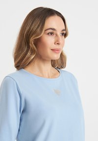 Lichtblauw longsleeve shirt van zachte stof, met een zilveren hartdetail op de borst en een ronde hals.