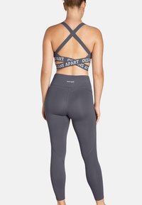 Grijze sportbeha met gekruiste bandjes en de tekst "OCEANS APART". Hoogsluitende grijze legging met een gladde textuur en subtiele stikdetails.