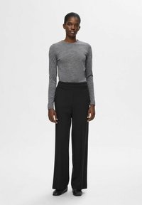 Grå långärmad topp och svarta vida byxor. Toppen har ett texturerat tyg, medan byxorna har en slät yta. Svarta skor fulländar outfiten.
