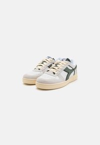 Hvite skinnsneakers med grå semsket skinndetaljer, grønt side-logo og beige gummisåler. Har runde lisser og perforert tådesign.