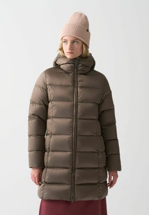Bruine pufferjack met horizontaal gequiltte secties, hoge kraag en ritsluiting. Het model draagt een lichtroze gebreide muts.