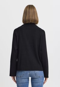 Maglione nero a maniche lunghe con collo alto, realizzato in tessuto morbido. Presenta una vestibilità comoda e cuciture delle spalle scese, indossato con jeans azzurri chiari.