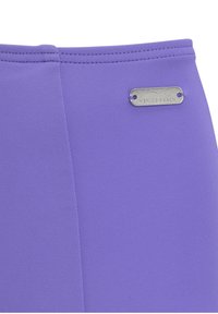 Pantaloni sportivi viola con una superficie liscia, dettagli di cuciture e un'etichetta metallica argentata con la scritta "VENICE BEACH."