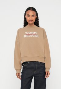 Καφέ φούτερ με ψηλό λαιμό και μακριά μανίκια, με λευκό και κόκκινο κεντητό λογότυπο "TOMMY HILFIGER" στο στήθος.