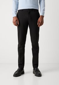 Pantalons noirs ajustés avec une coupe slim, présentant une texture lisse et des poches avant. Assortis avec des mocassins noirs pour un look complet.