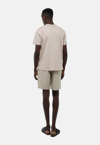 T-shirt en coton beige et shorts kaki clair, vus de dos. Le t-shirt a une coupe classique et les shorts comportent des poches latérales. Sandales noires.