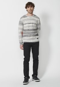 Pulover tricotat cu dungi gri și albe, din material texturat, cu manșete și tiv cu dantele; asortat cu pantaloni slim-fit negri și adidași negri.
