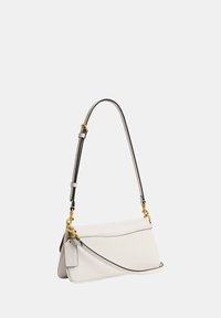 Sac à épaule en cuir blanc avec bandoulière ajustable, ferrures dorées, bordure noire et une étiquette en cuir fixée près de la poignée.