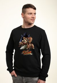 Felpa nera con una stampa grafica di due personaggi di Street Fighter, caratterizzata da colori vivaci e espressioni facciali dettagliate.