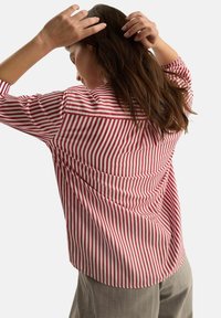 Czerwono-biała bluzka w paski o lu�źnym kroju, z długimi rękawami i detalem na plecach. Wykonana z lekkiej tkaniny.