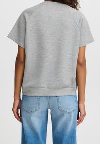 Grå, kortärmad sweatshirt med avslappnad passform, ribbat nederkant och en mjuk textur, tillsammans med ljusblå vida jeans.