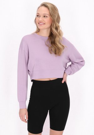 Sweatshirt scurt lila cu mâneci lungi, guler rotund și textură fină, asortat cu pantaloni scurți negri de ciclism cu talie înaltă.