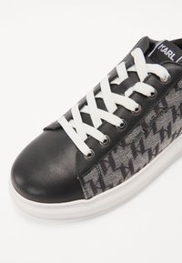 Sneaker nera con punta in pelle liscia e lato in tessuto grigio a fantasia. Presenta lacci bianchi, occhielli in metallo e suola in gomma bianca.