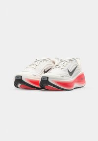 Chaussures de course avec une tige en maille blanche et grise, logo swoosh noir, semelle rose vif et noire, et détails texturés sur la maille.