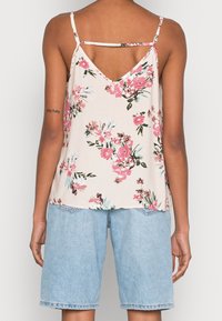 Donna che indossa un top senza maniche floreale rosa e bianco con spalline sottili e pantaloncini di jeans leggeri blu. Vista da dietro.