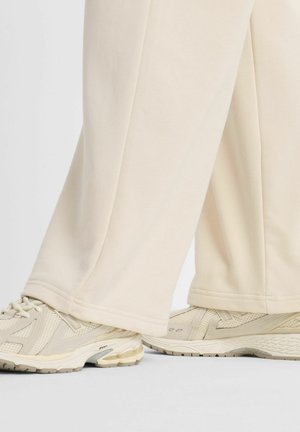 Pantaloni sportivi color crema, dalla vestibilità ampia, con una texture liscia e un orlo semplice, abbinati a scarpe da ginnastica beige chiaro con pannelli in mesh.
