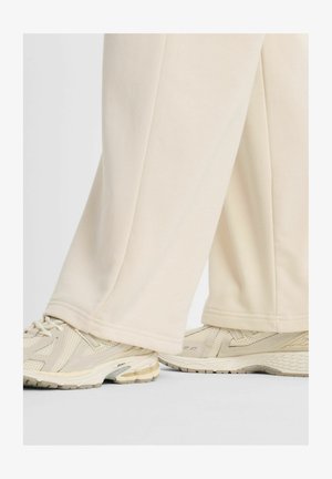 Pantaloni sportivi color crema, dalla vestibilità ampia, con una texture liscia e un orlo semplice, abbinati a scarpe da ginnastica beige chiaro con pannelli in mesh.