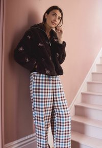 Juoda, pūkuota zip-up striukė su gėlių siuvinėjimu, derinama su plačiomis pločio kelnių mėlynoje, baltos ir burgundijos spalvų atspalviuose. Matomi minkšti tekstūros.