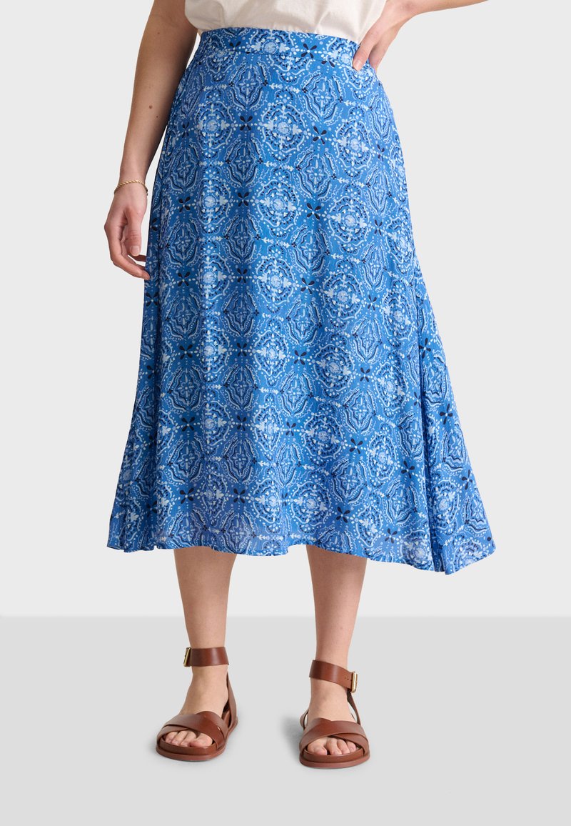 Jupe bleue à motif avec un design évasé, présentant des motifs complexes et un tissu lisse, assortie à des sandales brunes.