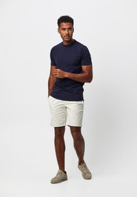 Marineblaues Kurzarm-T-Shirt, cremefarbene Shorts und beigefarbene Sneakers; lockere Passform, glatte Textur und klare Linien.