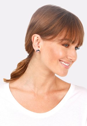 Pendientes circulares de stud en negro y rosa exhibidos en un modelo con cabello en capas; los pendientes presentan un acabado brillante y un diseño único en forma de media luna.