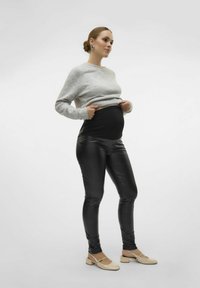Zwarte, high-waisted leggings met een glanzende afwerking, gecombineerd met een lichtgrijze trui. Model draagt huidskleurige block-heeled schoenen.